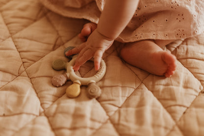 Baby's hand  holding the silicone teether from the Tiny Firsts Bundle
